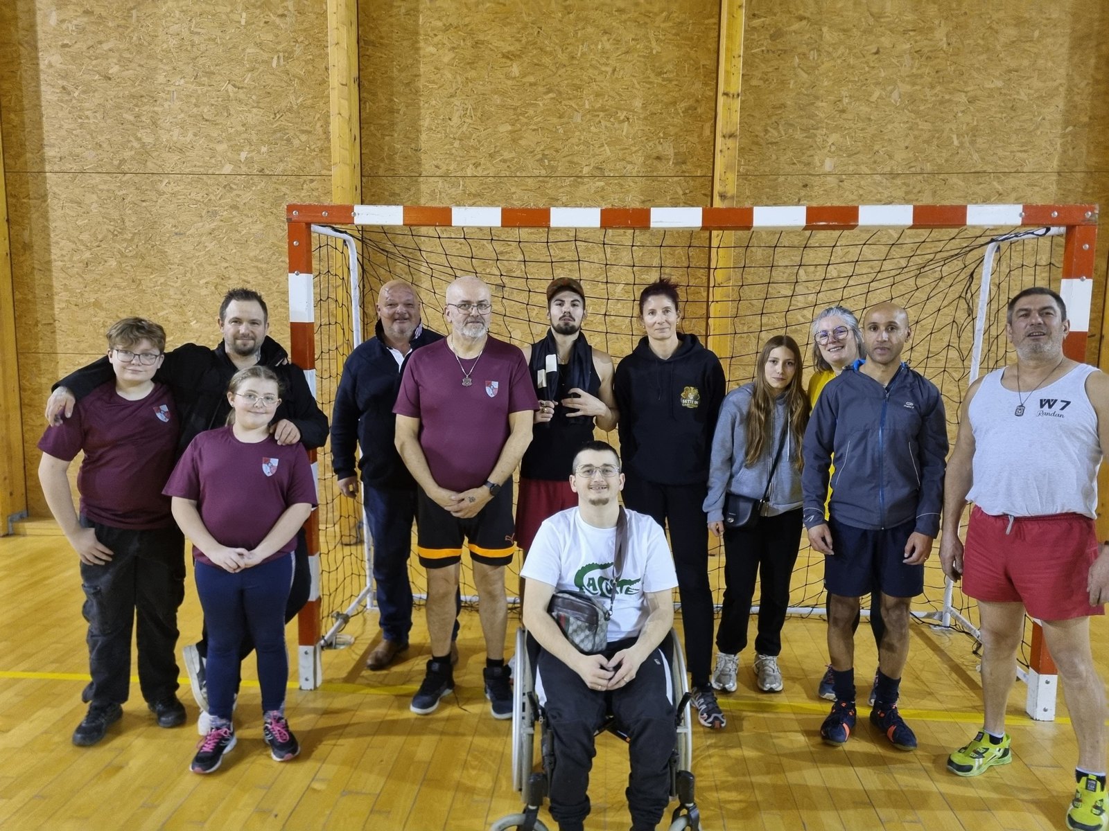Le groupe pose dans un gymnase devant un but, avec des participants debout et en fauteuil.