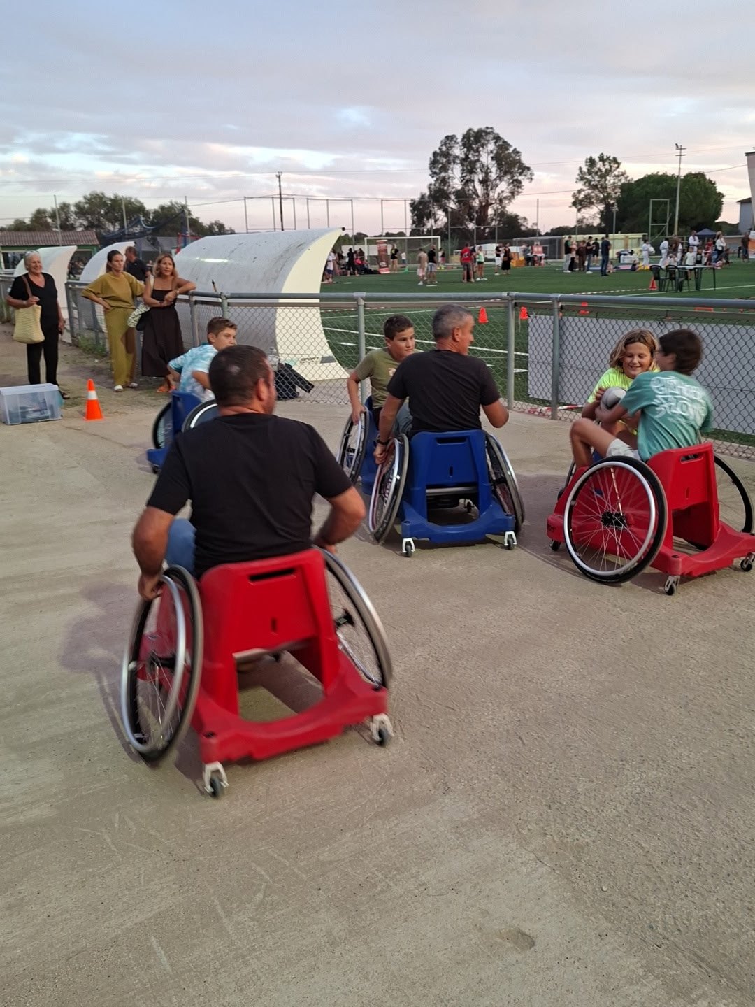 Plusieurs participants en fauteuil sont réunis sur un espace sportif en plein air.
