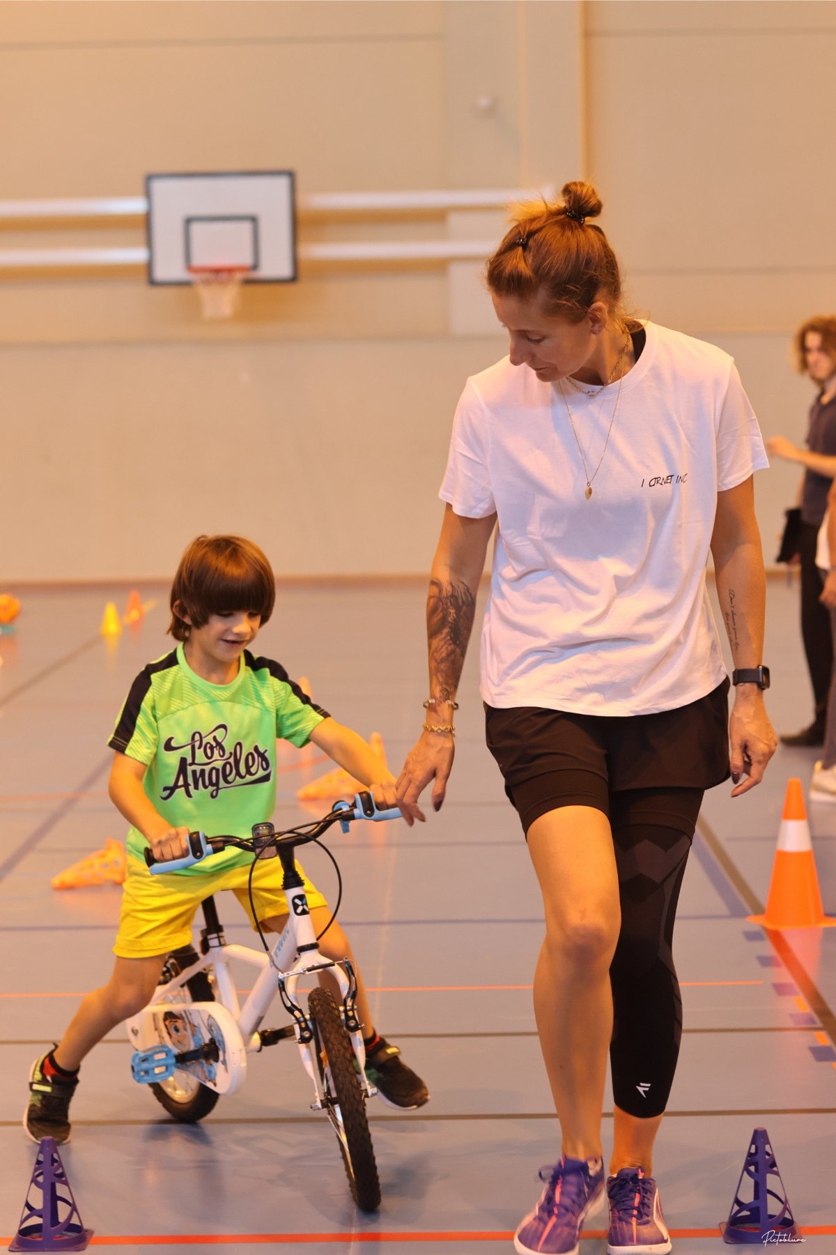 Une adulte accompagne un enfant dans la découverte d’un fauteuil sportif au gymnase.